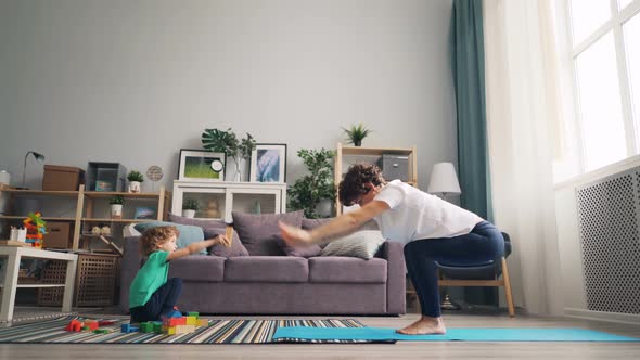 Beautiful Mother Doing Yoga at Home and Watching Her Son Playing with Toys alt