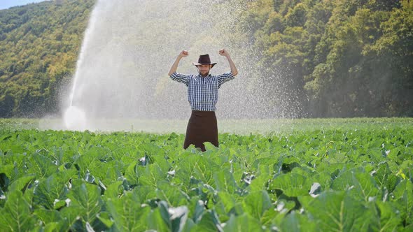 Rarmer Standing in Plantation and Raises Hands Up. Happy Farmer Enjoying Success alt