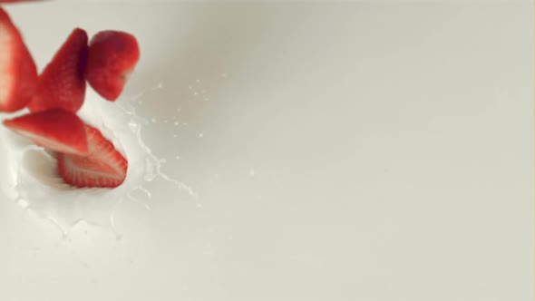 Super Slow Motion Sliced Into Pieces of Strawberries Falls Into the Milk alt