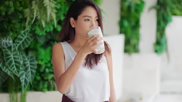 Attractive Asian woman drinking milk and smiling at home alt