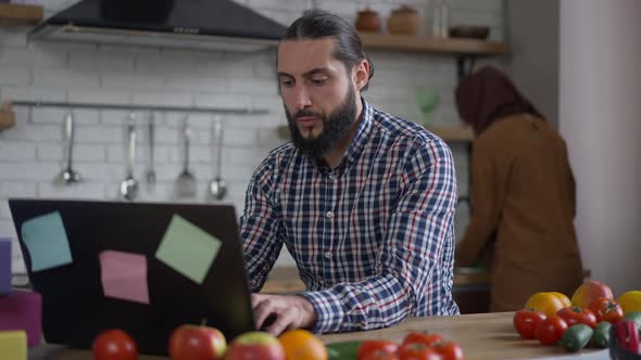 Portrait of Busy Handsome Middle Eastern Man Messaging Online Typing on Laptop Keyboard with Blurred alt