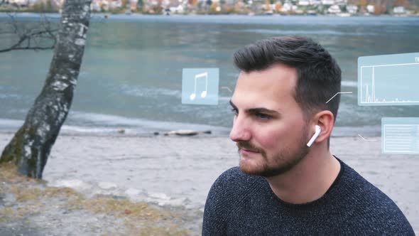 Young man sitting on the shore of a mountain lake and listening to music - digital generated hologra alt
