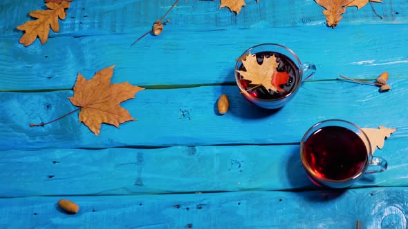 Cozy Autumn Background With A Cup Of Tea On An Old Wooden Table, Leaves Are Blown Away By The Wind