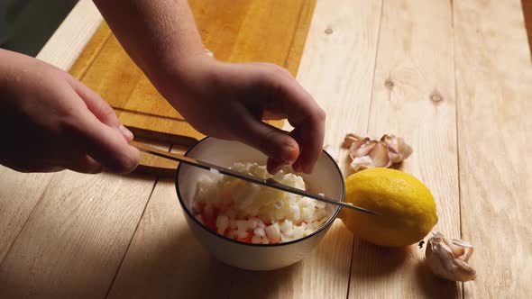 A woman's hands use a knife to transfer sliced onions from a cutting board to a bowl of sliced alt