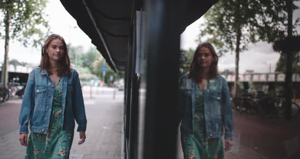A young woman is walking on the street looking at herself in a store - window alt