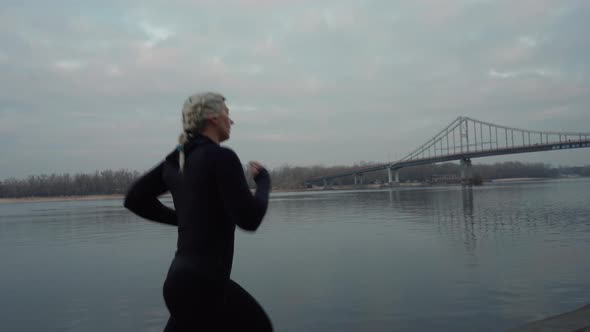 Sportswoman Running Near River in Evening alt