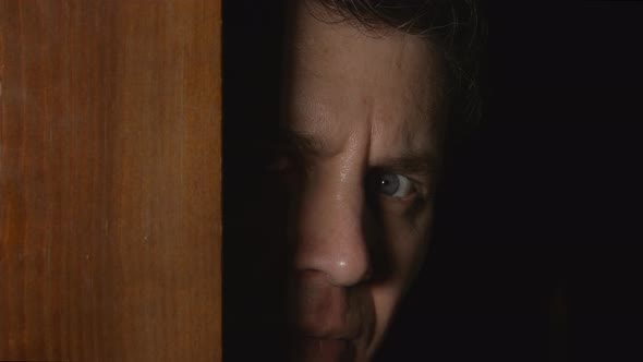 Human male face looks from a door from the darkness
