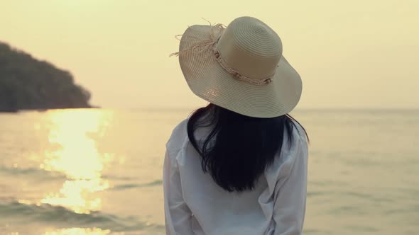 Attractive Asian woman wearing fedora hat standing on the beach looking at sea view. alt