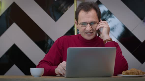 Handsome Middleaged Businessman Talking on Mobile Phone Working in Cafe