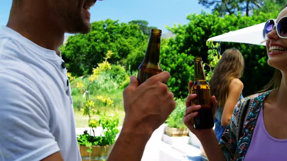 Couple interacting while having a bottle of beer near poolside alt