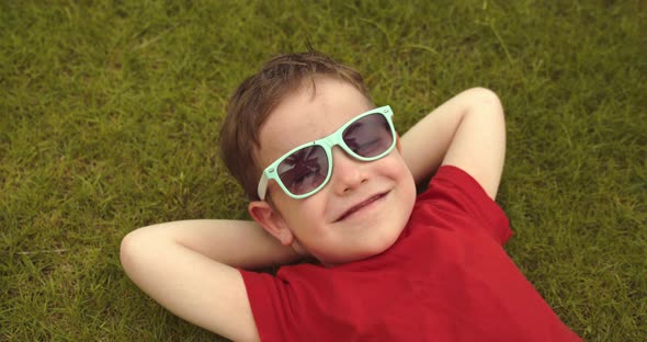 Happy Cute Little Boy Lies on the Green Grass a Child in Sunglasses Lies on the Grass Resting alt