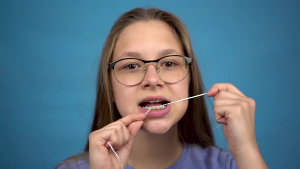 Girl with Braces Brushing Your Teeth with Dental Floss. A Girl with Colored Braces on Her Teeth alt