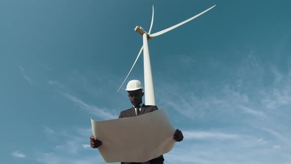 Man in Suit Standing Among Windmills with Blueprints alt