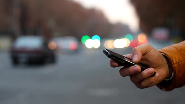 Closeup of Male Hand Using Cell Phone Near Highway