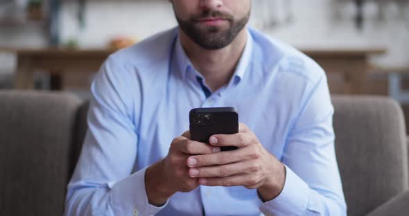 Portrait Shot of the Cheerful Young Man Taping While Texting on the Smartphone Device in the Living alt