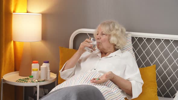Caucasian Senior Woman Taking Medicines and Drinking Water While Lie on Bed Alone
