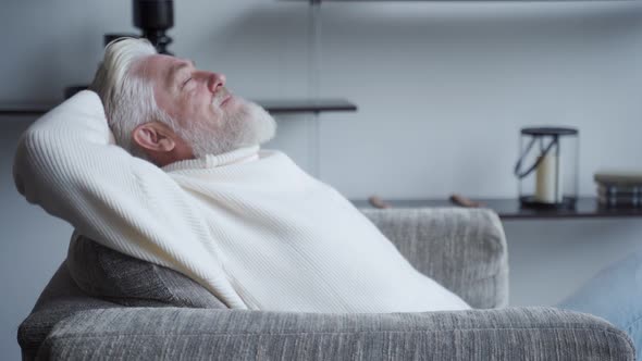 Relaxed Mature Man with a Gray Beard at Home Sitting in a Chair alt