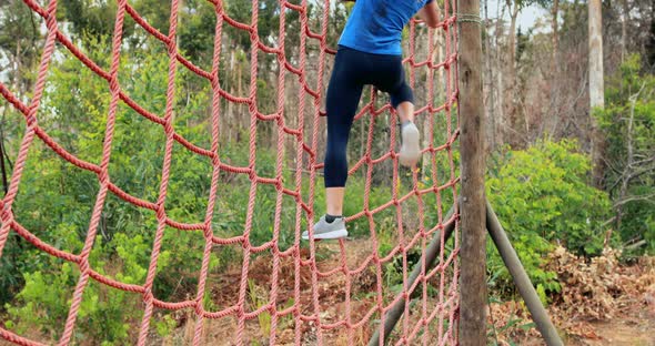 Fit woman climbing a net during obstacle course alt