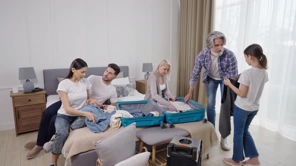 Family Helping Grandfather to Pack Clothes Into Suitcase Before Plane Flight alt