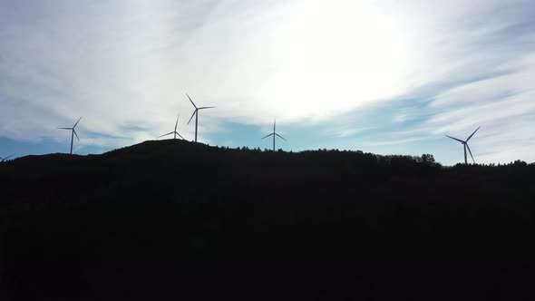 Silhouette of wind turbines against bright sky with dark mountain foreground - 5 rotating turbines a alt