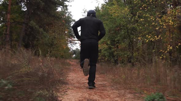 A Guy in Black Dress is Training Runs Through the Forest Among Pines Autumn