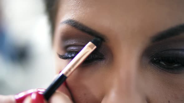 Closeup View of the Makeup Artist's Hands Using Brush to Paint Eyebrows for a Model with False alt