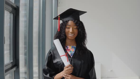 Young African American Female Graduate Standing in Front of the Camera with a Diplomas in Her Hands alt