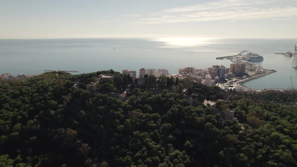 Aerial view Malaga Port with sunlight reflection from Mount Gibralfaro lush vegetation, Spain