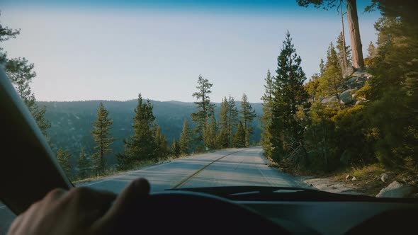 Beautiful First Person View of Male Hand Holding Car Steering Wheel Driving Along Mountain Road alt