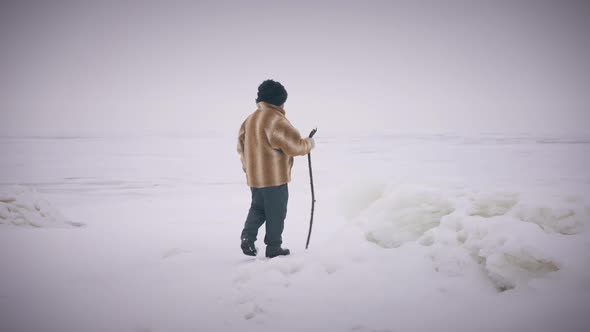 Wide Shot Winter Landscape with Indigenous Senior Man Walking with Stick in Slow Motion alt
