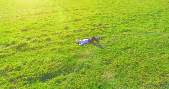 Low Orbital Flight Around Man on Green Grass with Notebook Pad at Yellow Rural Field alt