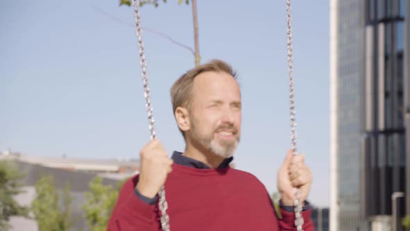 A Middleaged Handsome Caucasian Man Swings on a Swing with a Smile in an Urban Area alt