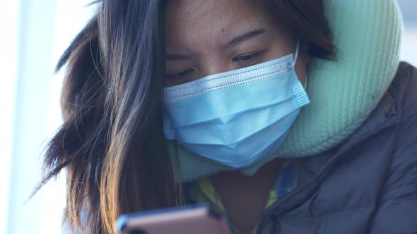 Close up of Asian woman wearing mask sitting and using smartphone at Airport