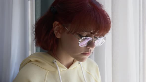 Closeup view on face of redhead teen girl near a window.