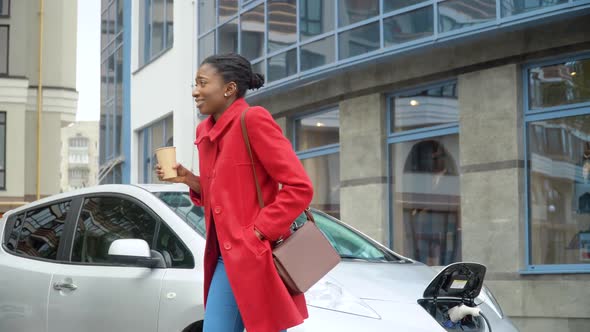 African American Girl Drinking Coffee Near Her Electric Car alt