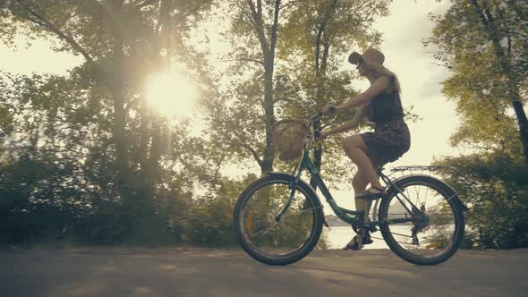 Cycling Female In Hat Riding On Summer Time At Sunset. Girl Rides Bicycle On Sunset. City Park. alt
