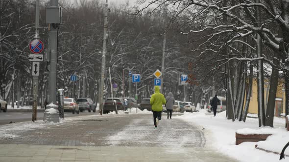 A Male Athlete Makes a Morning Jog Through the Streets of the City on a Cold Winter Day