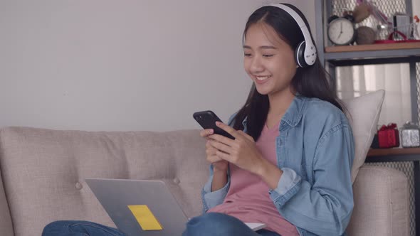 Attractive young Asian woman listening to music in headphones use smartphone.