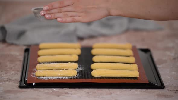 Sprinkle raw dough for eclairs on a baking sheet with powdered sugar.	