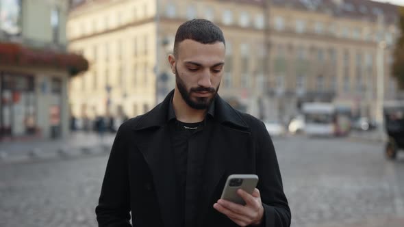 Confident Muslim Man Standing on Street with Mobile in Hands alt