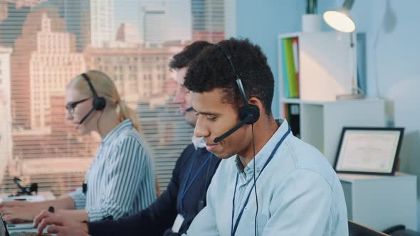 Close-up Shot of Smiling Mixed-race Man Taking Call in Busy Call Center