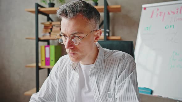 Concentrated Middle Aged Man in Eyeglasses Typing on Laptop Computer Working at Home Office Zoom Out alt