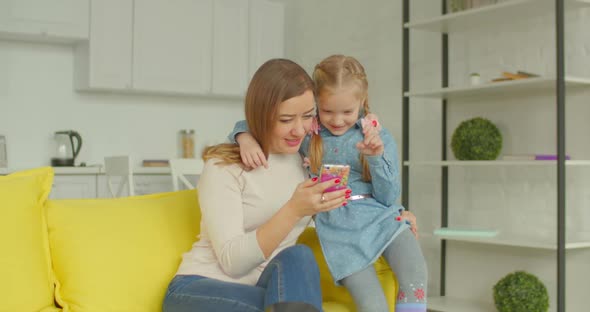 Mother and Cute Girl Browsing Online on Cellphone alt
