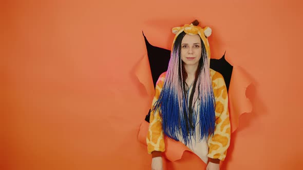 Young Woman in Pajamas of Giraffe in Hole of Orange Background alt