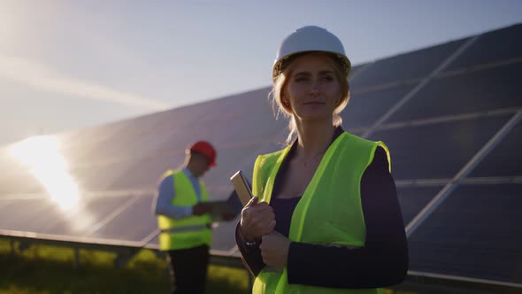 Portrait of a Female Solar Engineer Standing Looking at the Camera Another Man Near the Panels and alt