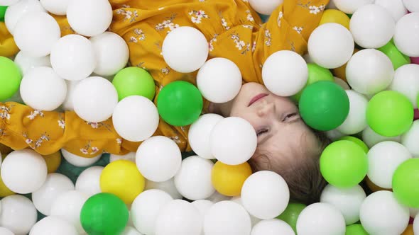 a Little Girl Plays in a Dry Pool with White Yellow and Green Plastic Balls alt