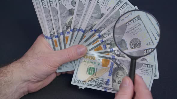 Person Checking Dollar Banknote for Authenticity with Magnifying Glass Close Up alt