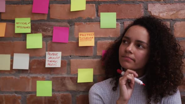 Thoughtful creative businesswoman writing on sticky notes in modern office alt