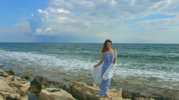 Happy Beautiful Woman Standing on Rocky Sea Beach, Foamy Waves Crashing Ashore alt