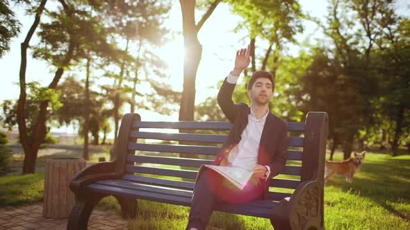 Slow Motion Handsome Business Man Sitting on Bench with Newspaper Seeing Friend and Raising Hand to